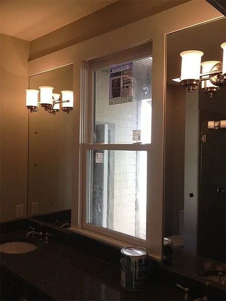 Public restroom with sinks, mirrors, and wall-mounted lights reflecting a window.
