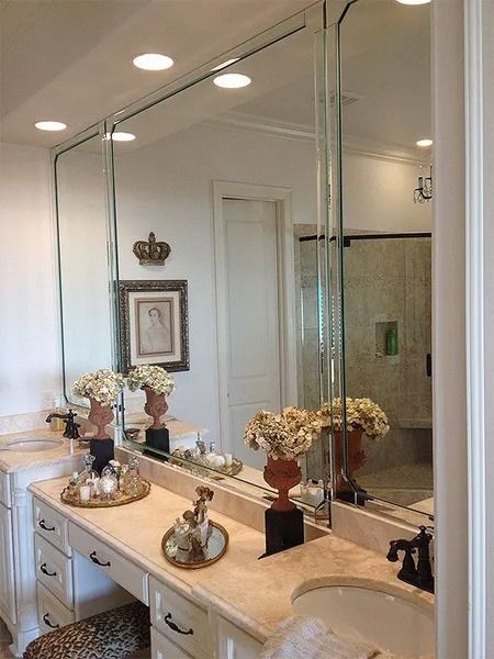 Elegant bathroom vanity with mirror, white cabinets, flowers, and wall sconces.