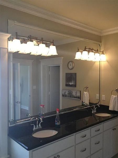 Bathroom vanity with black countertop, double sinks, large mirror, and bright vanity lights