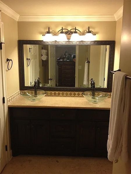 Bathroom vanity with double sinks, large mirror, and wall lights above a dark cabinet.
