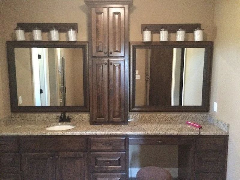 Bathroom vanity with two mirrors, dark wood cabinets, granite countertop, and built-in central storage cabinet.