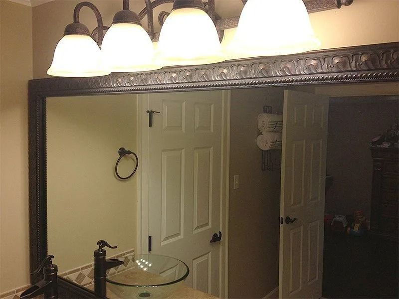 Bathroom vanity mirror with four lights, reflecting a white door and glass sink in a beige room