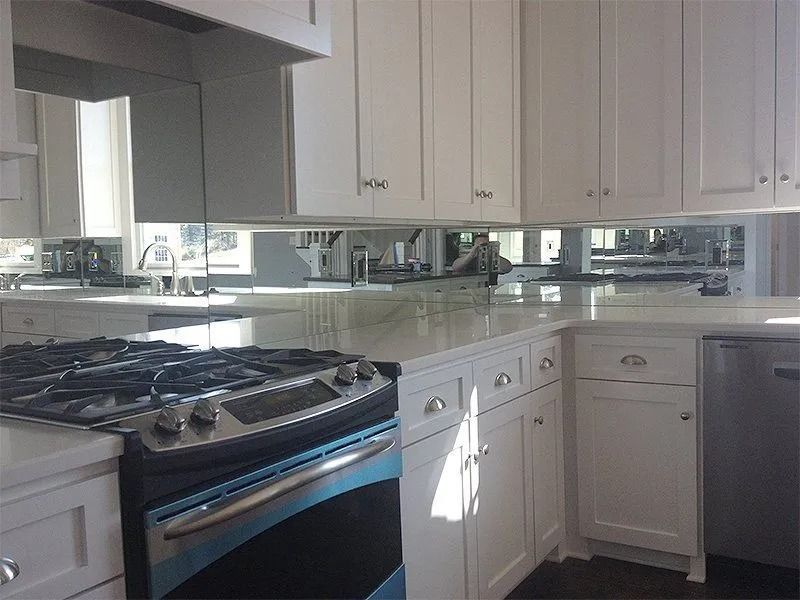 Bright white kitchen with black stove, white cabinets, and a reflective countertop.