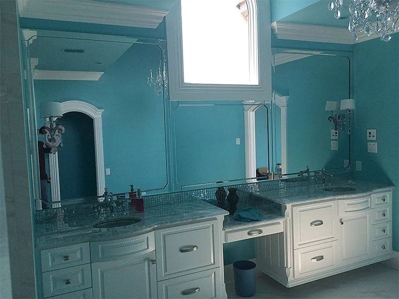 Blue bathroom with double vanity, large mirror, and white cabinets under a bright window