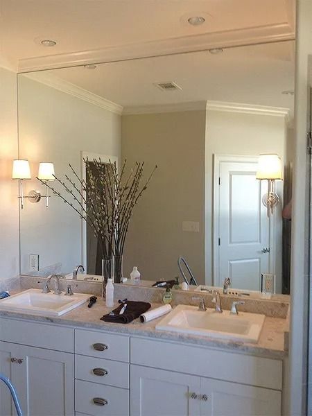 Bright bathroom vanity with double sinks, large mirror, wall sconces, and a vase of branches