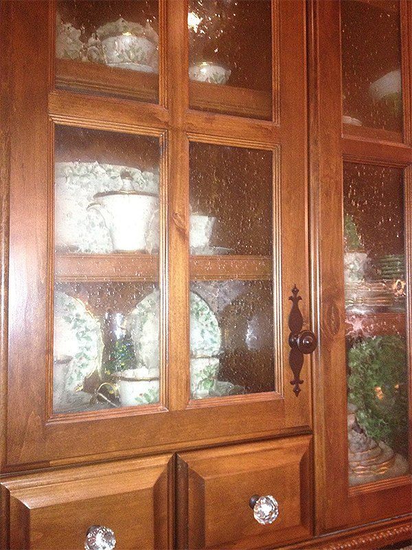 Wooden glass-front cabinet with china plates, bowls, and a decorative drawer knob