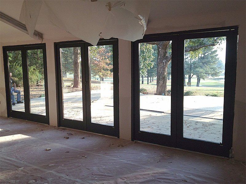 Empty room with large glass doors opening to a sunny outdoor patio and trees.