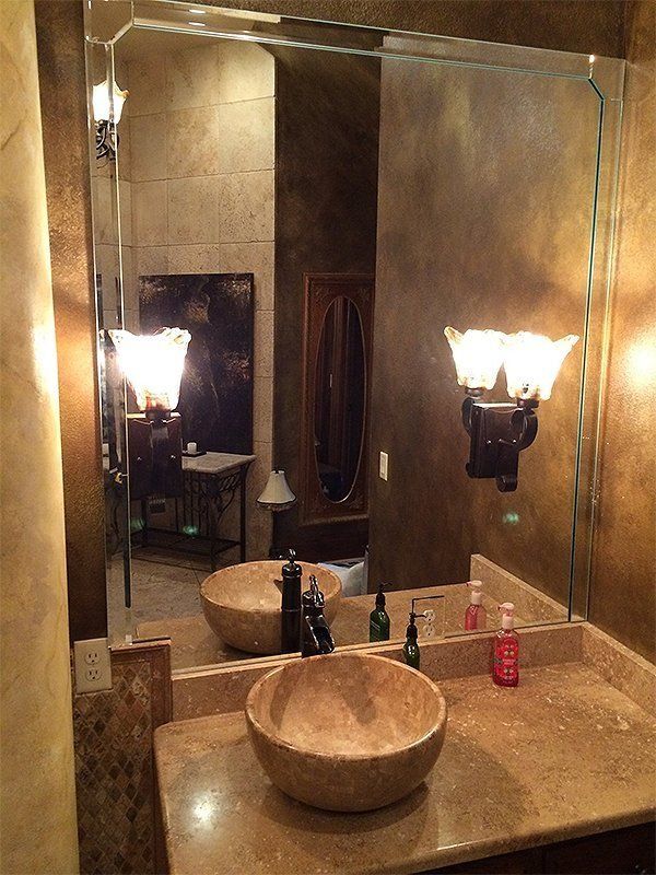 Bathroom vanity with round stone sink, large mirror, and warm wall sconces.