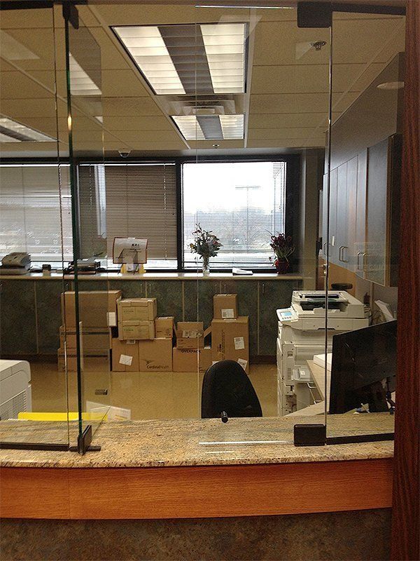 Glass-partitioned office reception with boxes, desk, and monitors behind a counter.