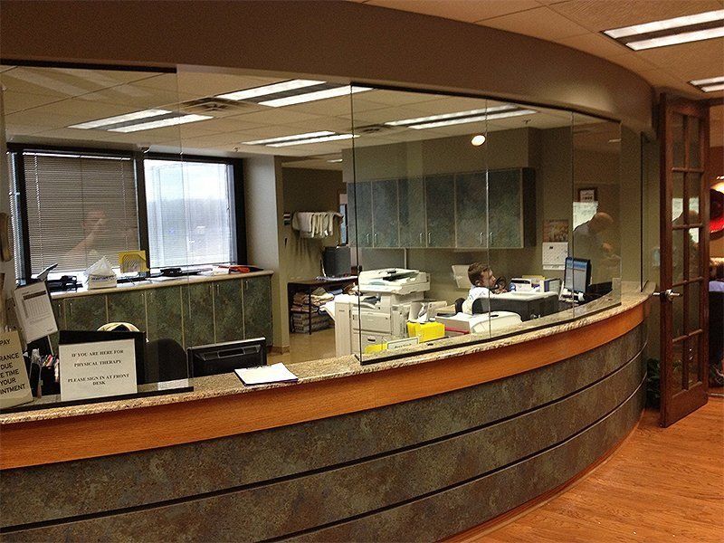Curved office reception desk with computer monitors, paperwork, and glass partition windows