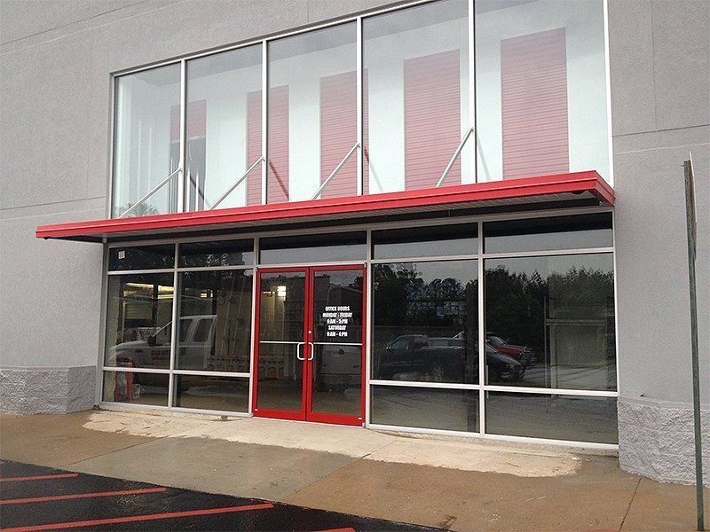 Storefront entrance with red-framed glass doors and windows under a red awning on a gray building