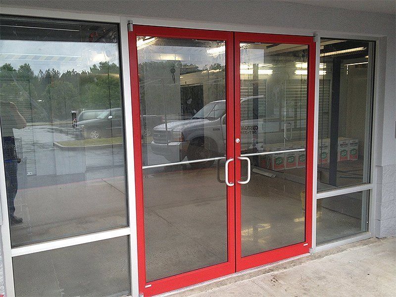 Red-framed glass double doors at a storefront entrance with reflections on the windows.