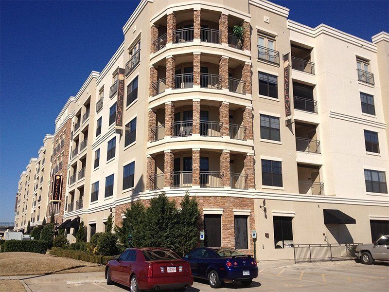 Apartment building with brick and cream facade, balconies, and parked cars on a sunny street