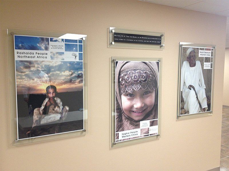 Three framed posters on a beige wall, featuring portraits and a landscape scene.