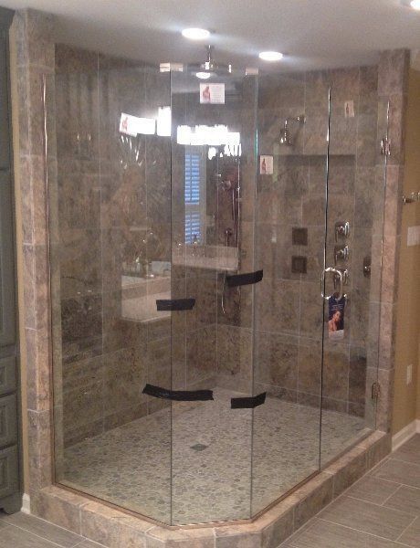 Glass shower enclosure with marble walls and a tiled floor in a bathroom.