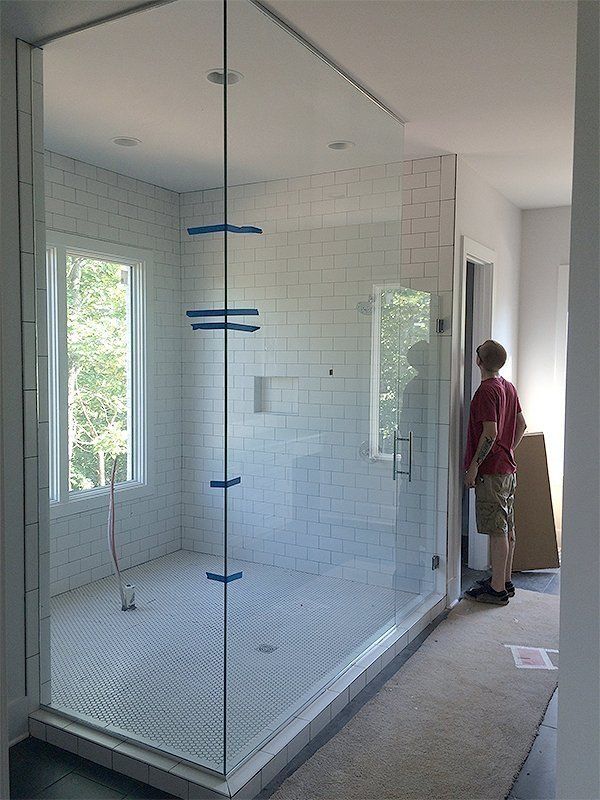 Modern glass shower enclosure in a white-tiled bathroom, with a person standing near the doorway.