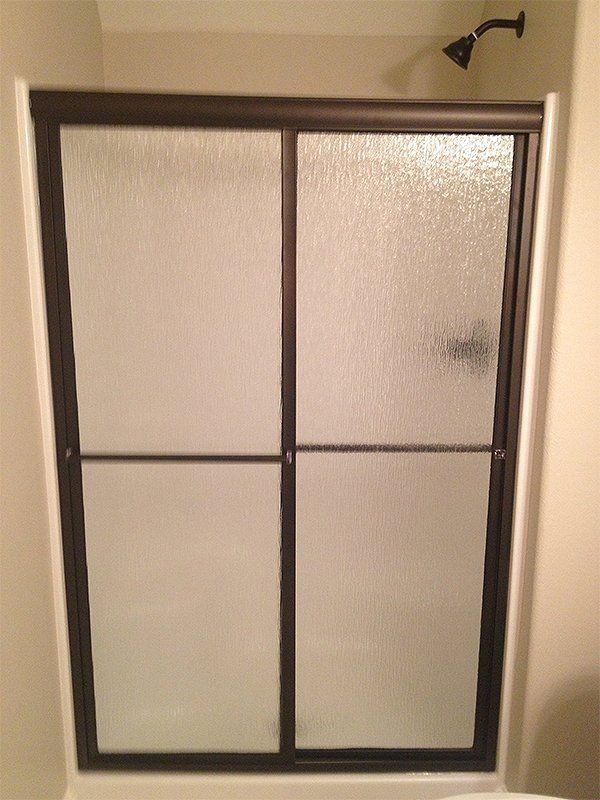 Framed frosted glass shower door with black trim and a top-mounted handle in a bathroom