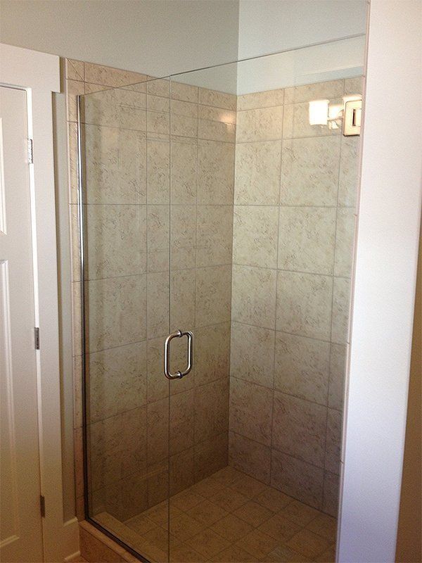 Glass shower enclosure with beige tile walls and a chrome handle in a bathroom
