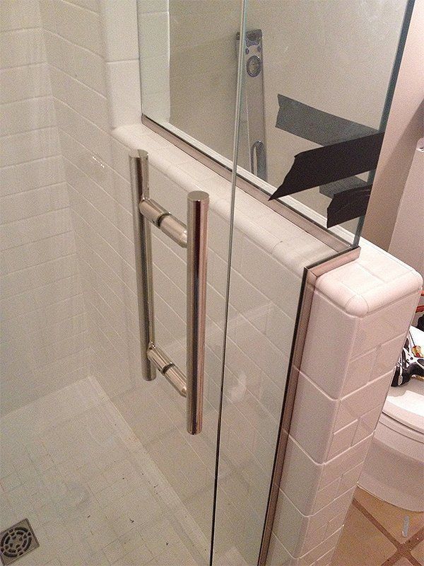 Glass shower door with chrome grab bars in a tiled bathroom