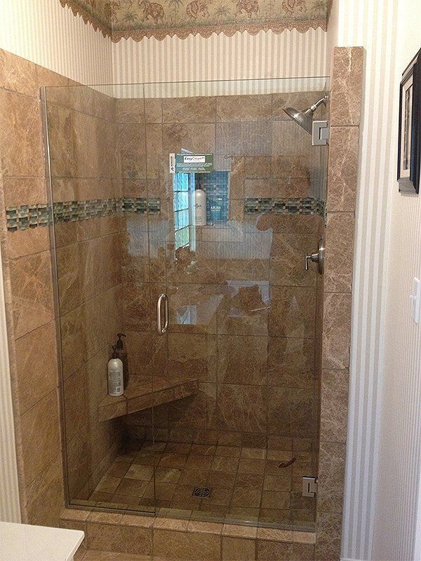 Tiled shower stall with glass door in a beige bathroom, with a wall-mounted showerhead and decorative border.