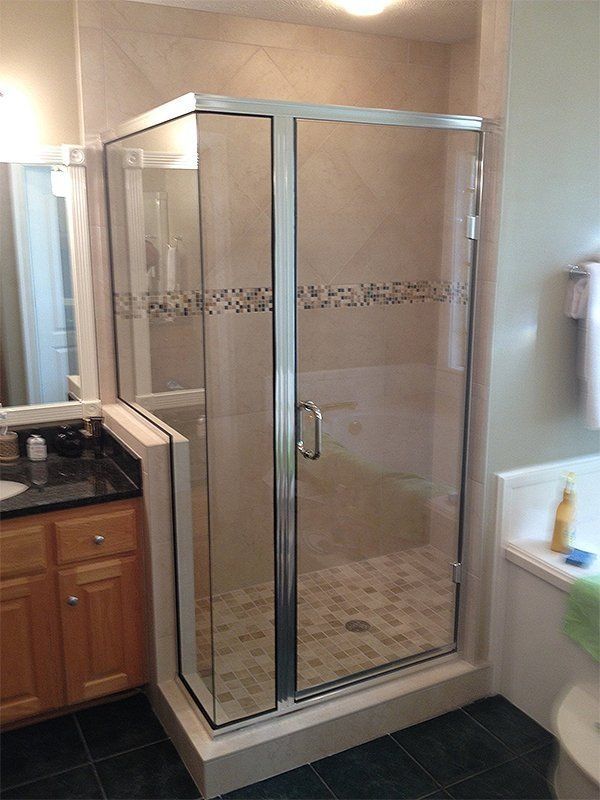 Glass-enclosed shower stall with chrome frame in a beige bathroom next to a vanity.