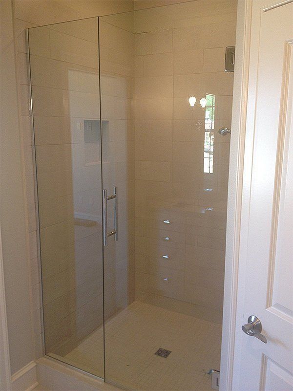Modern bathroom shower with clear glass enclosure, beige tile walls, and a white door