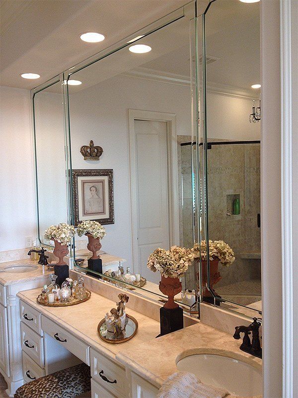 Elegant bathroom vanity with dual mirrors, white cabinets, marble countertop, and floral decor.