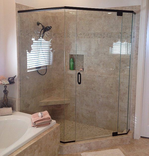 Corner glass shower enclosure in a beige-tiled bathroom with a bathtub and folded towels nearby