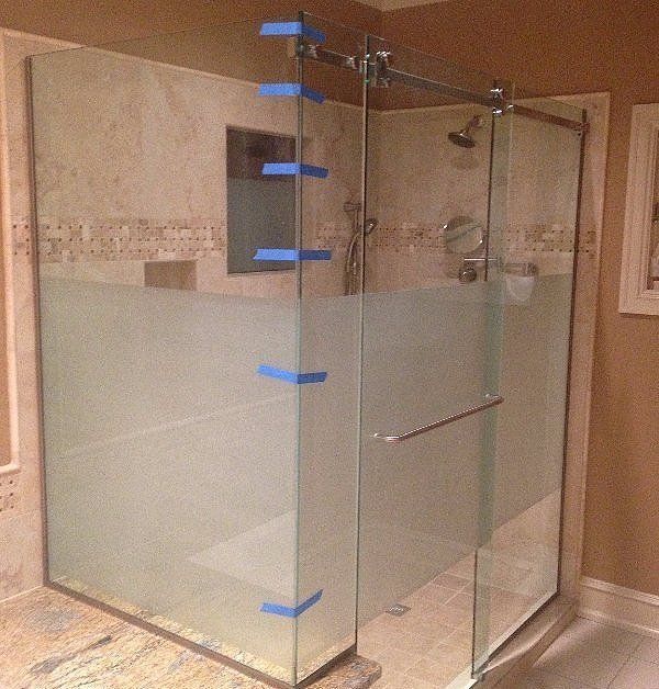 Glass shower enclosure with frosted lower panels and blue painter’s tape in a bathroom.