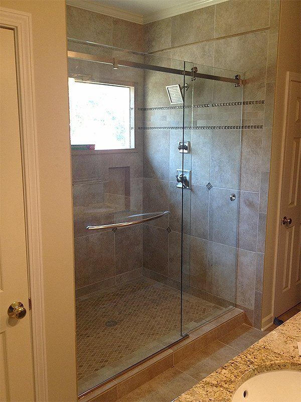 Glass-enclosed tiled shower with sliding door and brushed metal fixtures in a bathroom