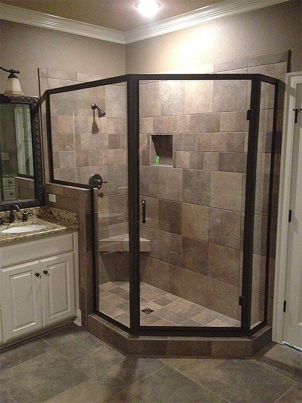 Corner shower with dark framed glass doors and tiled walls next to a bathroom vanity and mirror