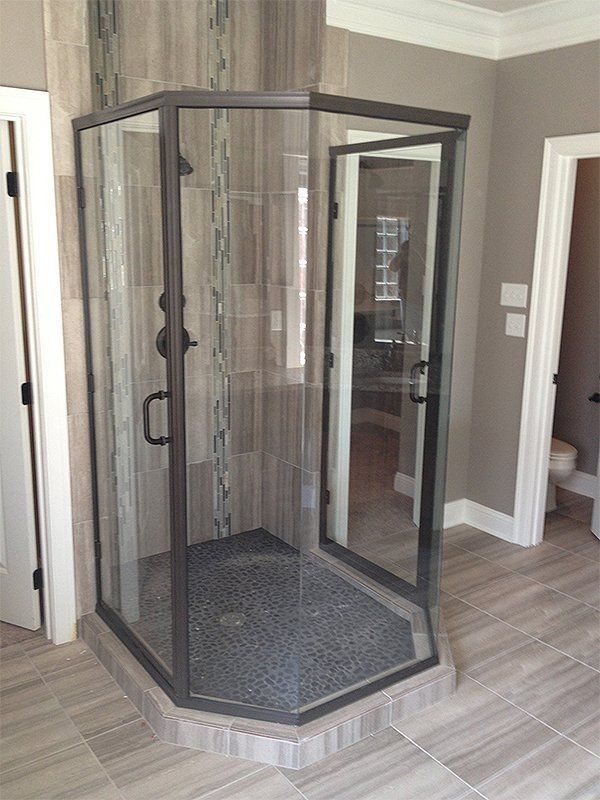 Glass corner shower with black frame in a tiled bathroom hallway