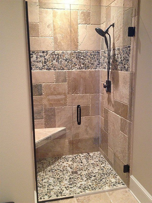 Empty tiled shower stall with glass door, built-in bench, and black handheld showerhead.