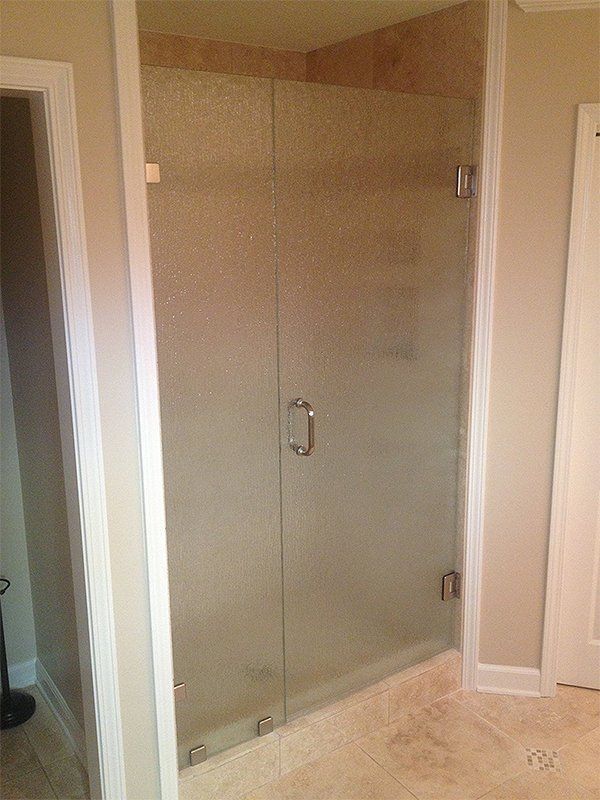 Corner glass shower enclosure in a beige tiled bathroom