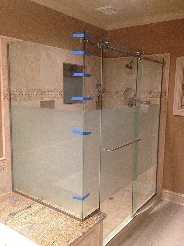 Glass walk-in shower with frosted lower panels and chrome hardware in a tiled bathroom