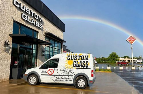 Custom Glass service van parked outside a storefront under a rainbow after rain