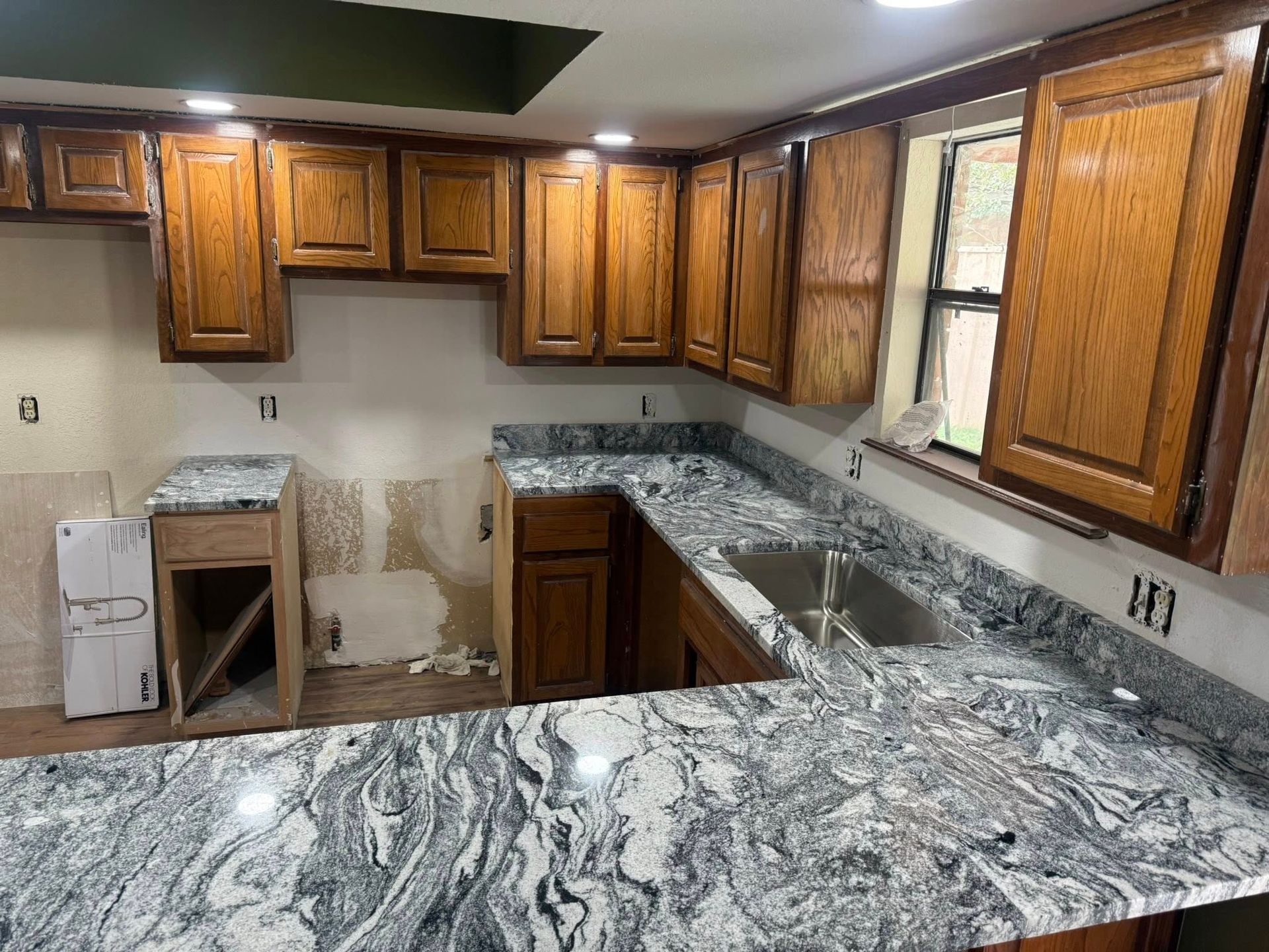 Kitchen with wood cabinets, granite countertops, and unfinished wall repairs near the sink and stove area