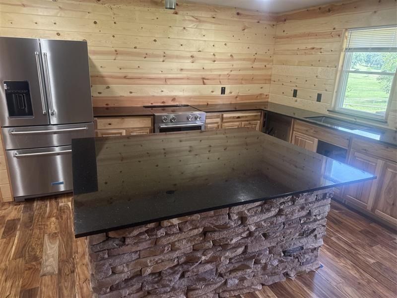 Modern kitchen with stainless steel appliances, wood-paneled walls, and a large dark island with stone base.