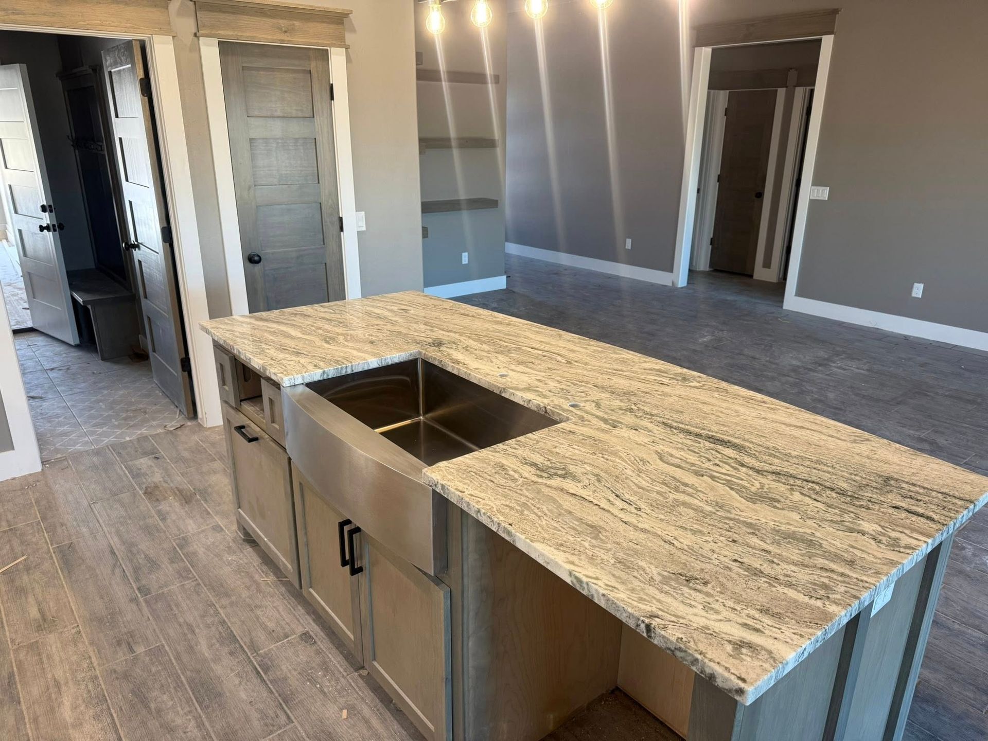 Modern kitchen with large granite island, stainless sink, gray walls, and wood-look flooring