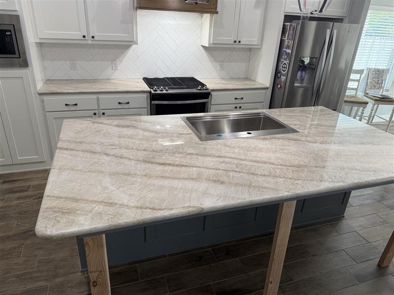 Modern kitchen with a large gray-veined island, stainless sink, white cabinets, and dark wood floor.
