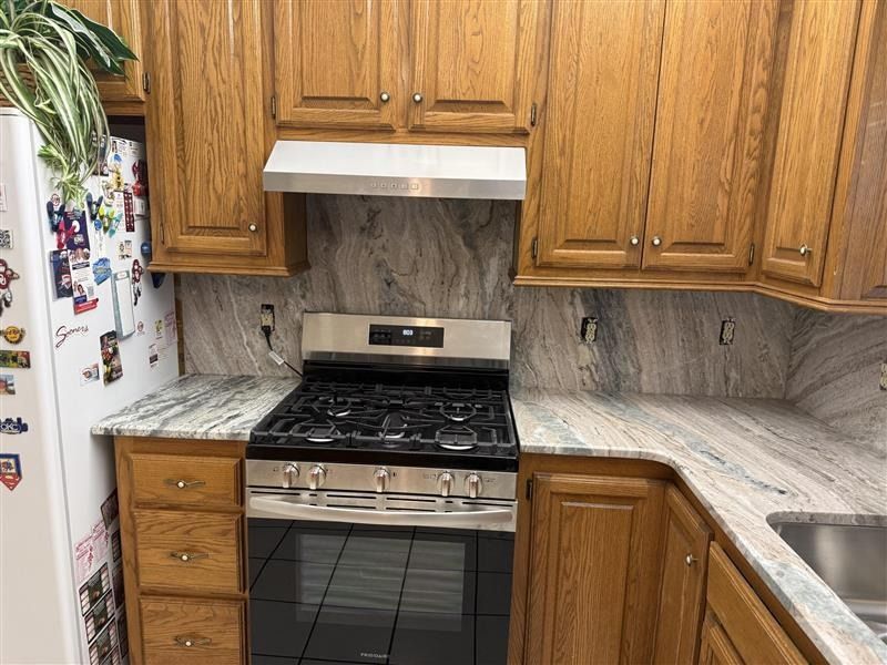Wooden kitchen with marble-look counters, gas stove, sink, and refrigerator covered in magnets.