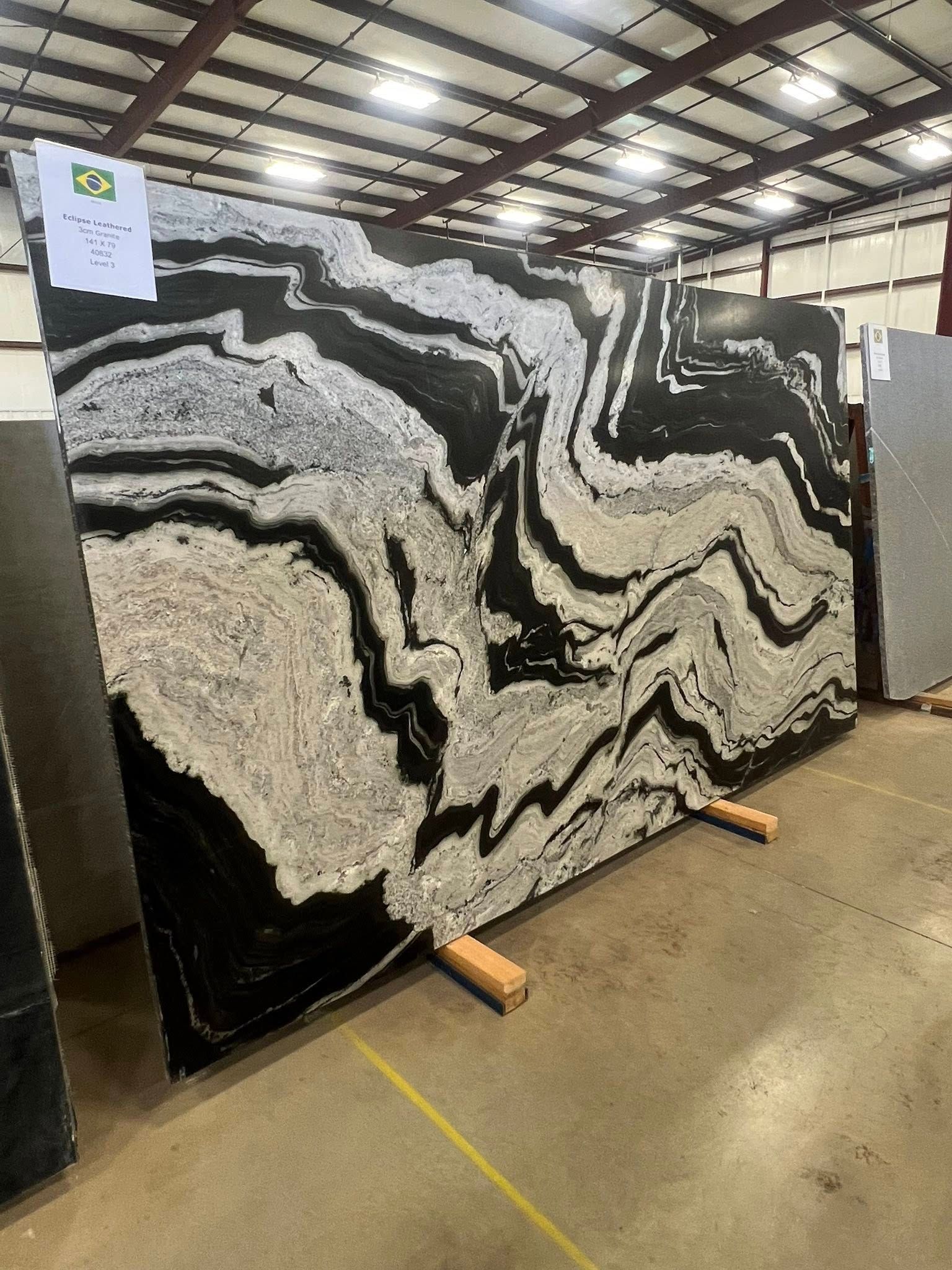 Large black-and-white veined stone slab standing upright in a warehouse on wooden supports