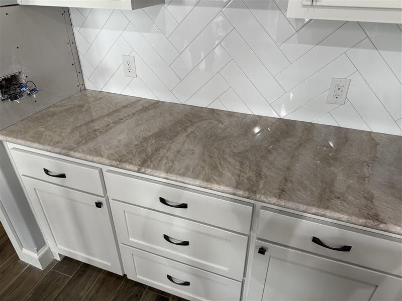 White kitchen countertop with gray marble look, white cabinets, and a white herringbone tile backsplash
