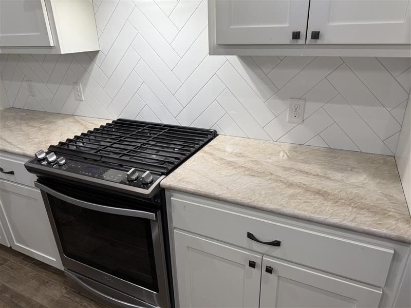 Modern kitchen with black stove, white cabinets, and light wood countertop against white tile backsplash