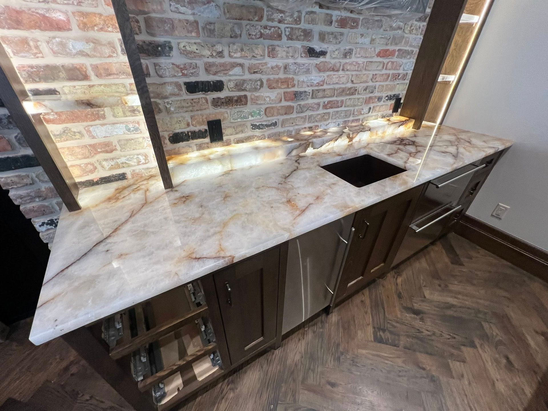 White marble kitchen counter with undermount sink and dark wood cabinets against a brick backsplash