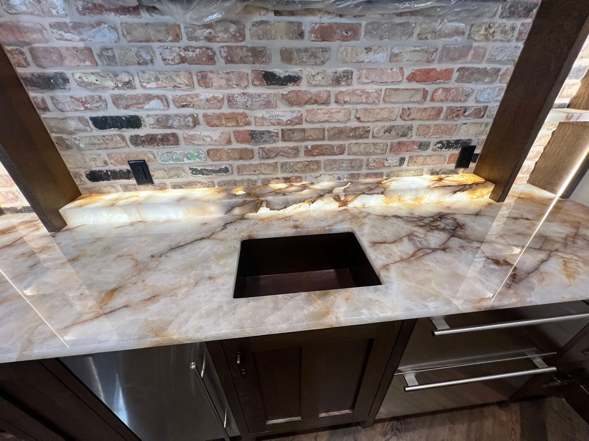 Marble countertop with black sink cutout against a brick backsplash and dark wood cabinets