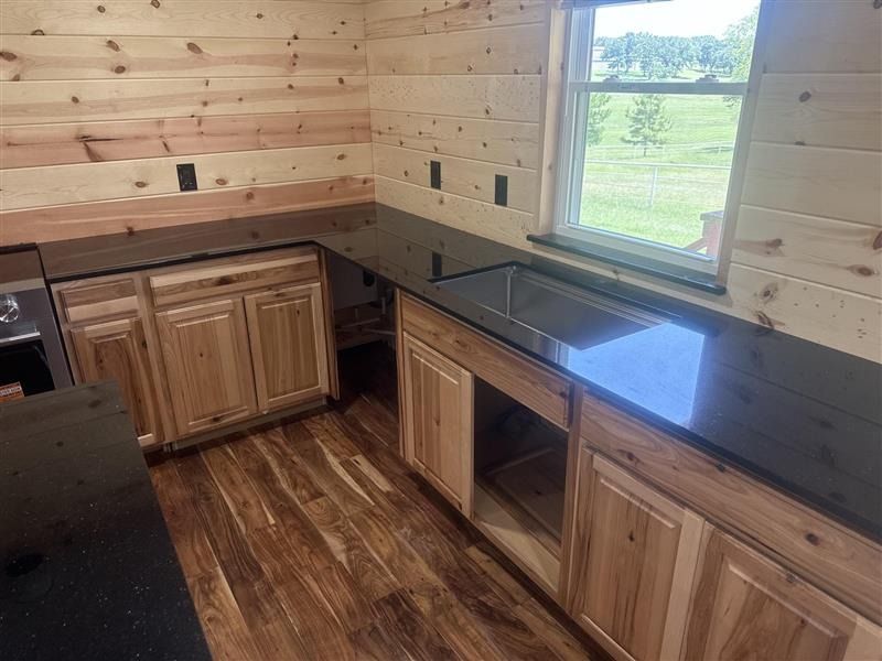 Wood-paneled kitchen with black countertops, wood cabinets, and a window above the sink