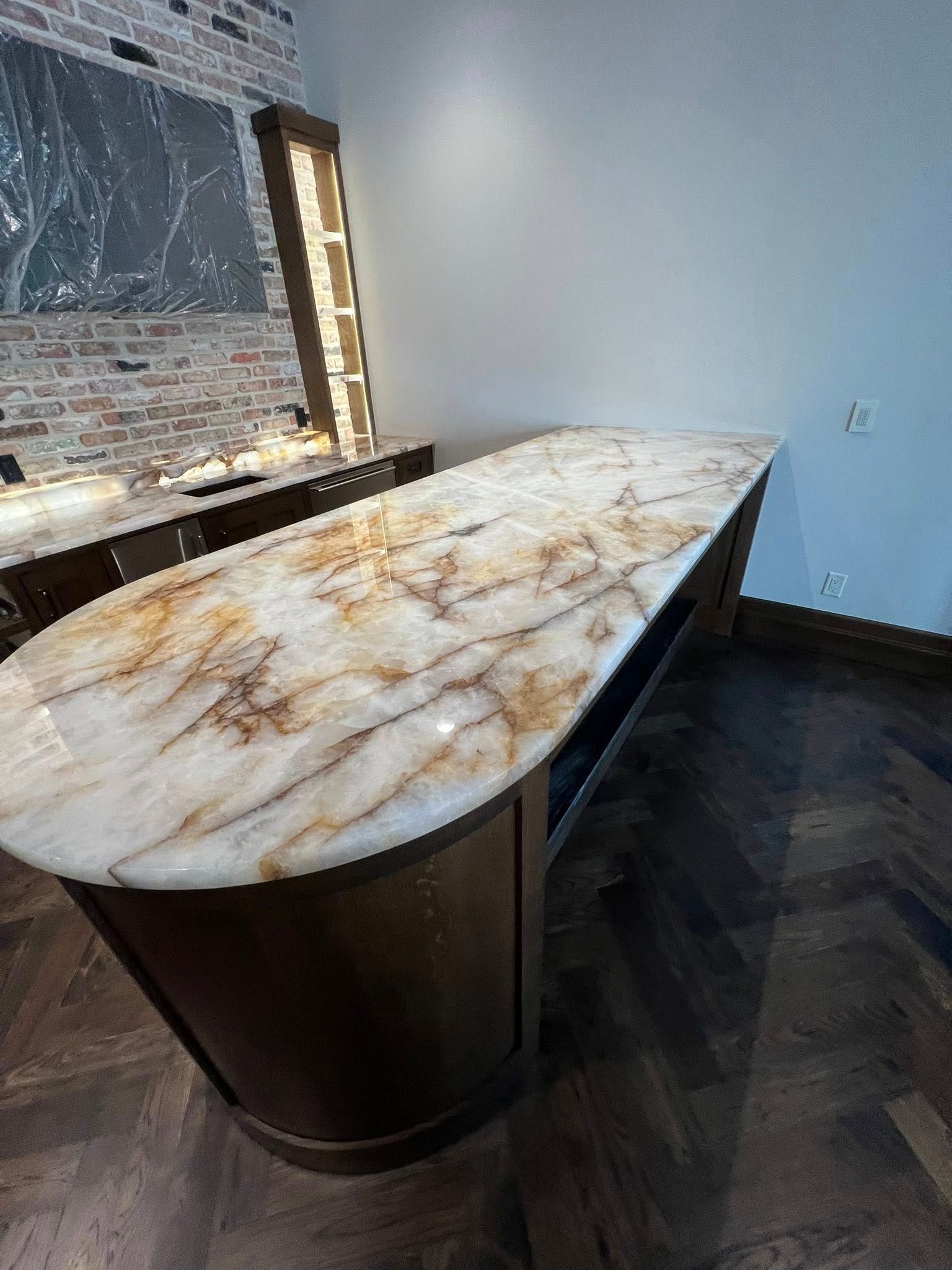 Modern kitchen with a long marble island countertop and dark wood base beside exposed brick wall.