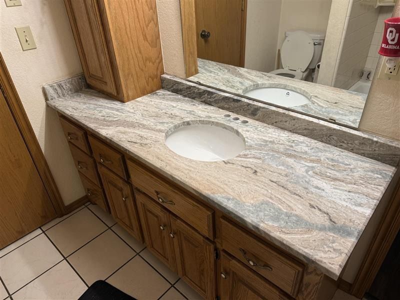 Bathroom vanity with double sinks, granite countertop, mirror, and wood cabinets.