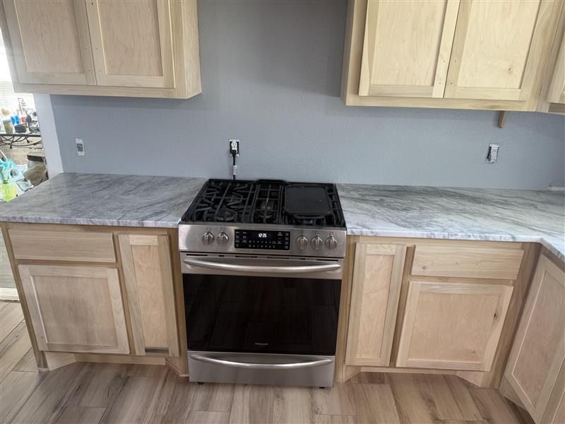Kitchen with light wood cabinets, gray walls, marble-look counters, and a stainless-steel gas range.